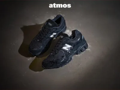 Promotional campaign image of the New Balance 2002R GORE-TEX in wet conditions, emphasizing waterproof performance with rain-speckled sneakers surrounded by Atmos, GORE-TEX, and New Balance branding on a dark backdrop