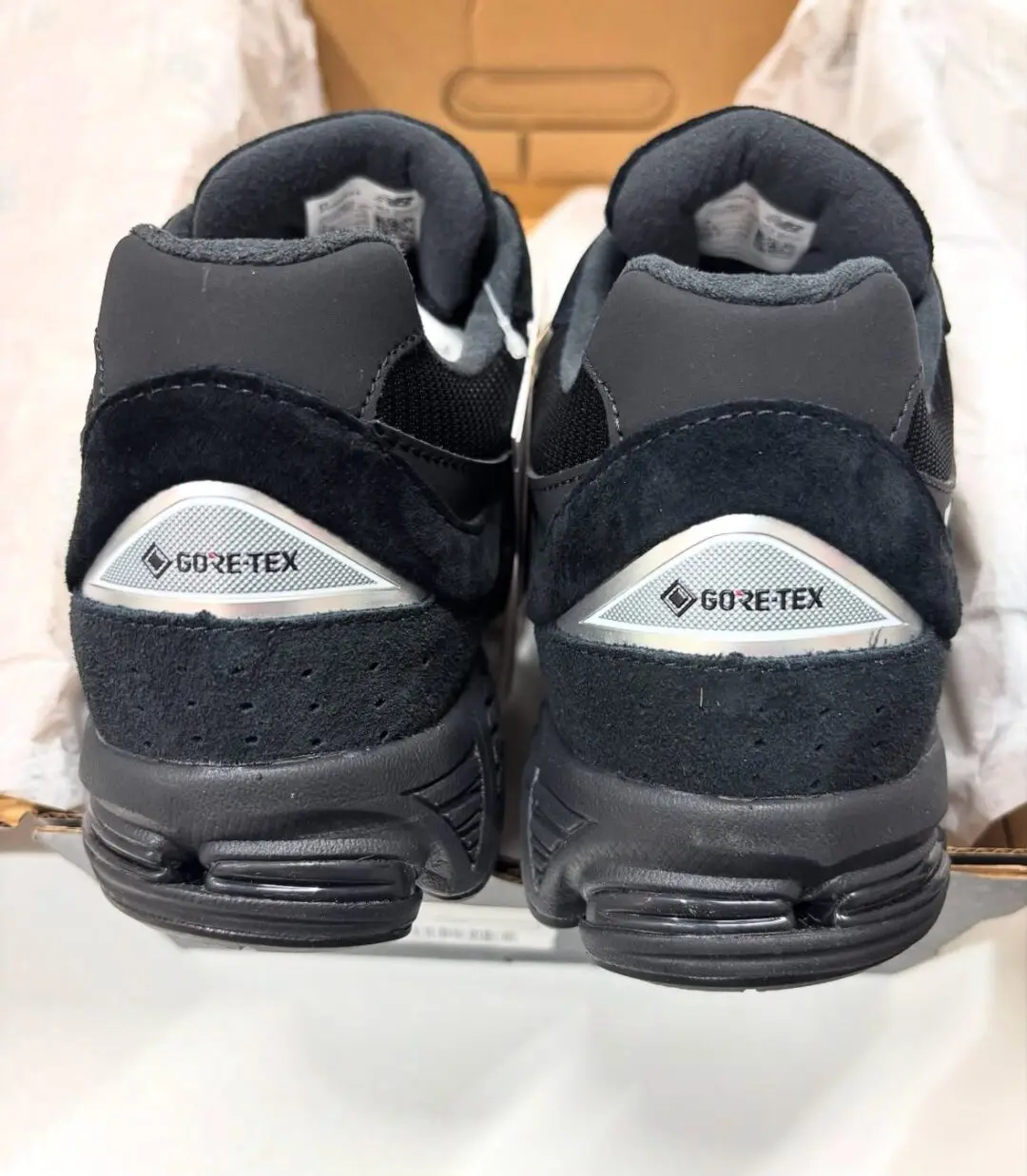 Rear view of the New Balance 2002R GORE-TEX in a black colorway, highlighting reflective silver GORE-TEX heel panels, premium black suede overlays, padded collars, and ABZORB heel cushioning while displayed inside the shoebox.