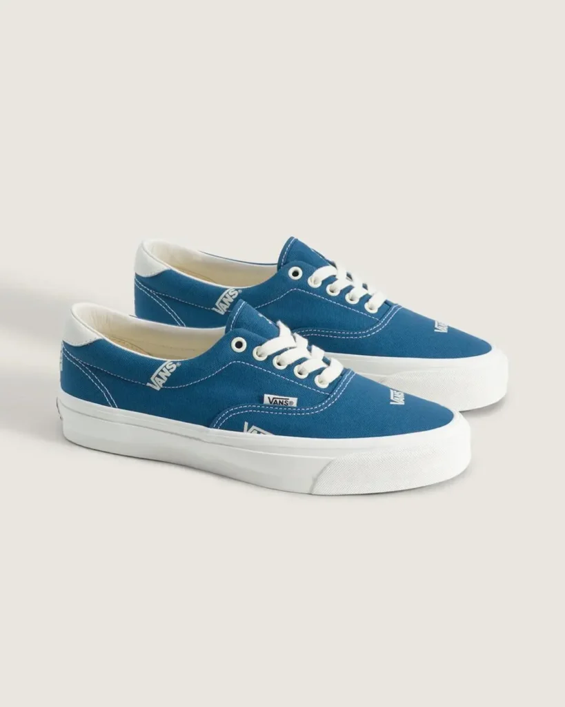 Pair of blue Vans OTW low-top canvas shoe featuring all-over white Vans logo graphics, white laces, contrast stitching, and white rubber foxing photographed in a clean studio set