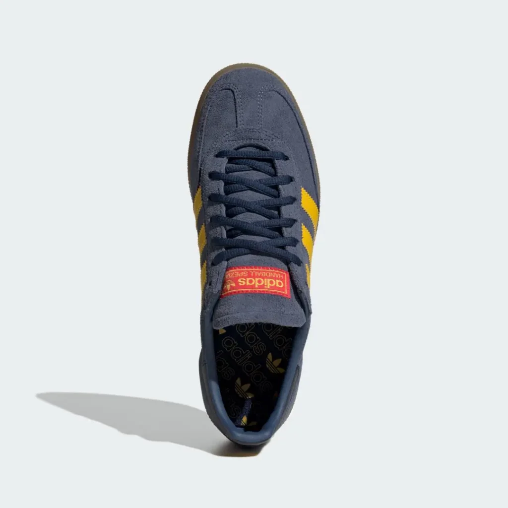 Top-down view of the adidas Handball Spezial highlighting the navy flat laces, textured suede upper, red woven adidas tongue label, and branded footbed with repeating Trefoil graphic