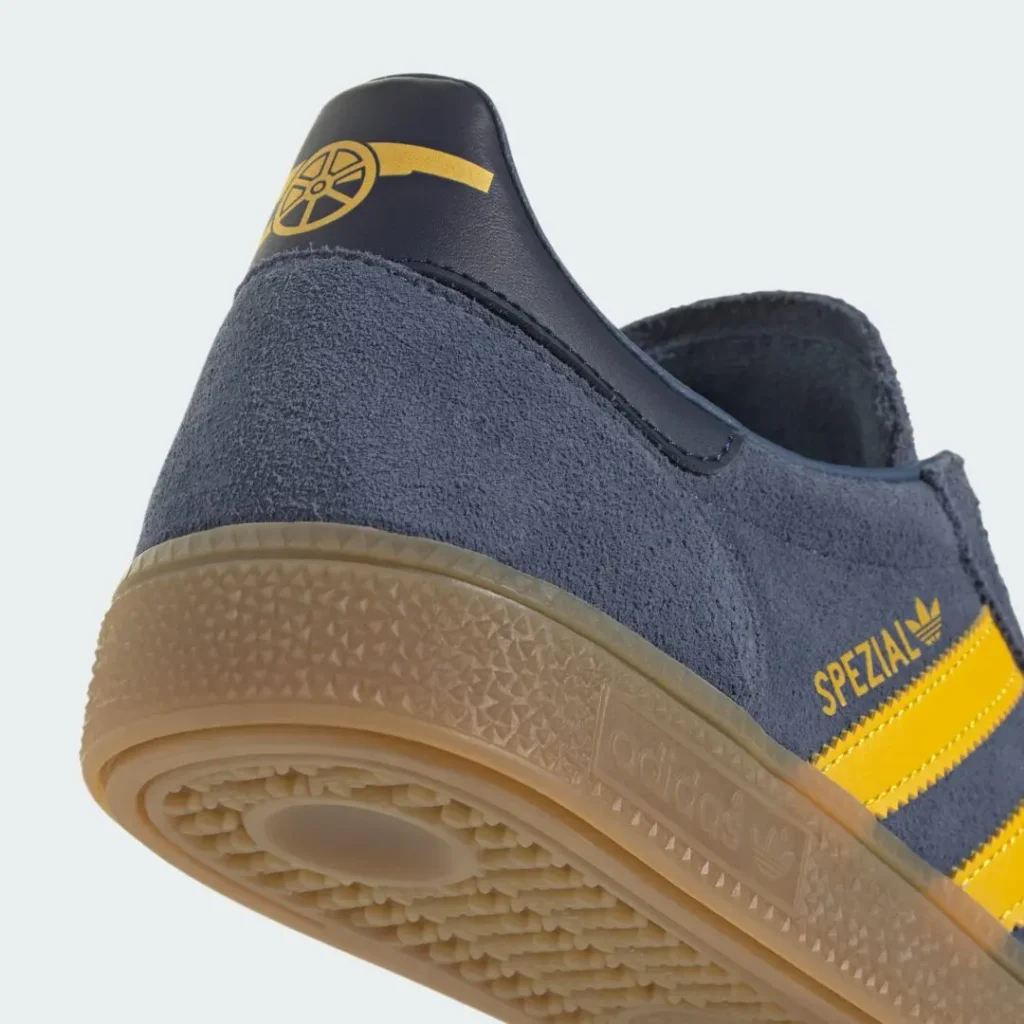 Close-up of the heel and outsole featuring the navy leather heel tab with a yellow Arsenal cannon logo, gold Spezial branding, textured gum midsole, and patterned gum outsole