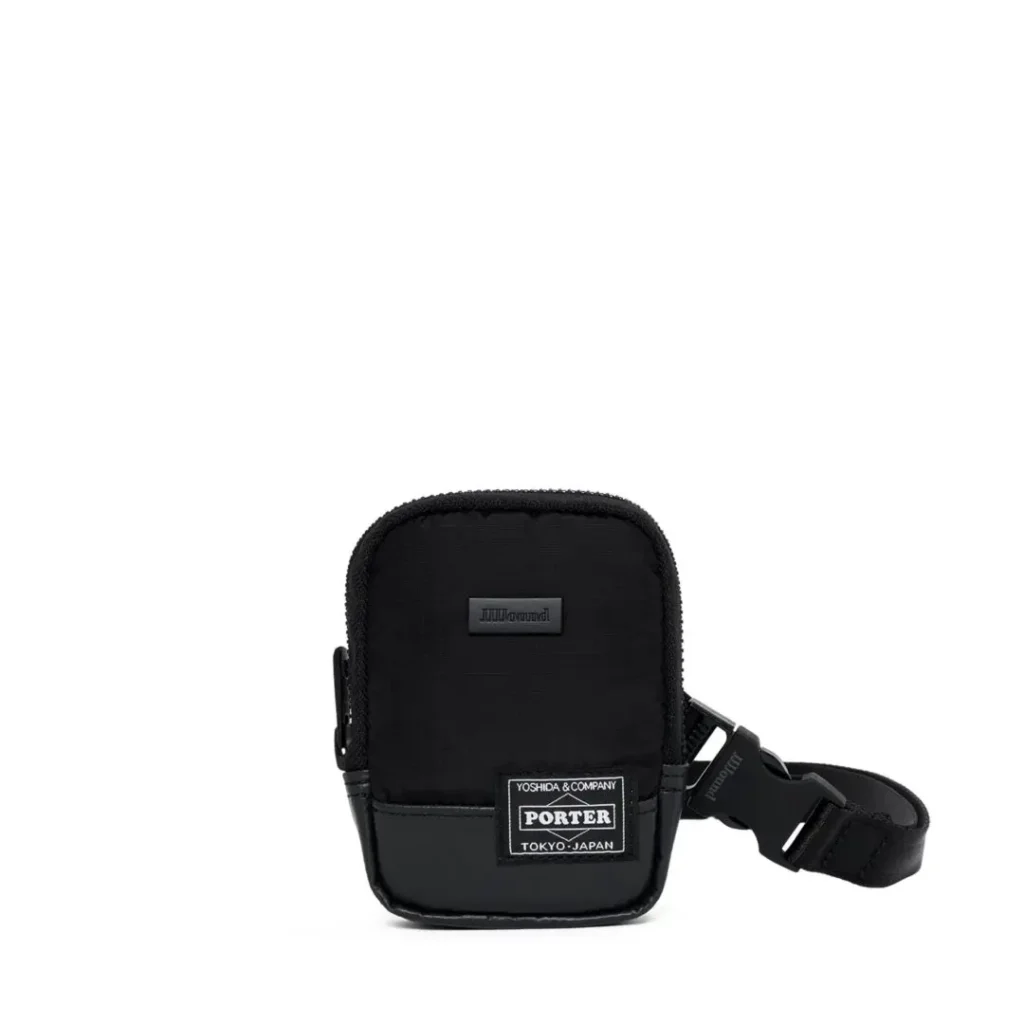 A black PORTER backpack hangs against a white wooden wall, highlighting its reflective front bungee cord, multiple zip compartments, side pockets, compression straps, padded shoulder straps, and reinforced bottom panel