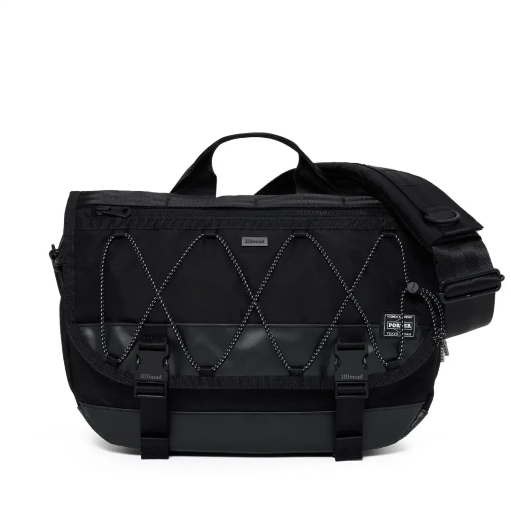 A black PORTER messenger bag with reflective bungee cord detailing, dual front buckle closures, flap design, adjustable shoulder strap, reinforced base, and woven logo patch is shown against a white background