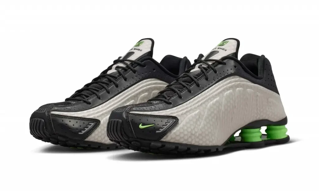 Pair of Nike Shox TL shoe in black and pearl gray with bright green Shox columns, shown in a three-quarter front view against a white background