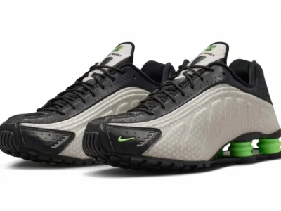 Pair of Nike Shox TL shoe in black and pearl gray with bright green Shox columns, shown in a three-quarter front view against a white background