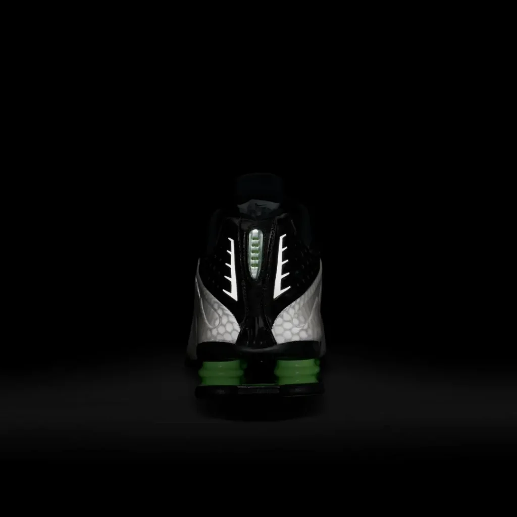 Rear studio view of the Nike Shox TL against a black background highlighting the reflective heel detailing and green Shox cushion