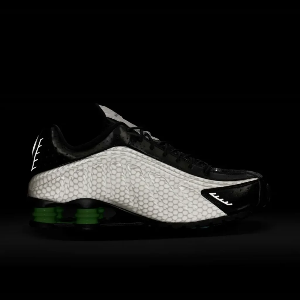 Studio side profile of the Nike Shox TL against a black background showcasing the textured pearl gray upper, black leather overlays, and bright green Shox column