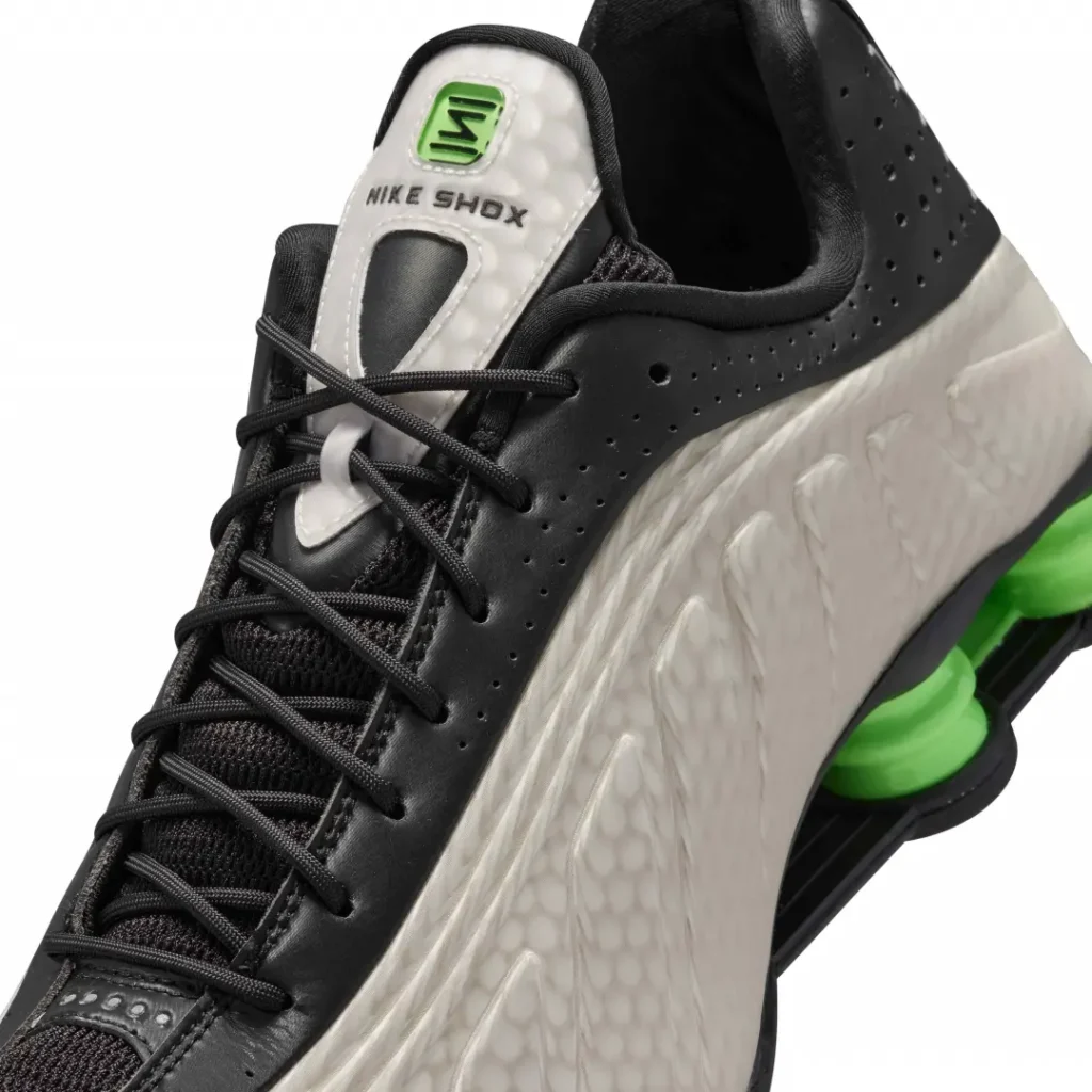 Close-up of the Nike Shox TL tongue, black leather eyestay, textured pearl gray upper, and green Nike Shox badge