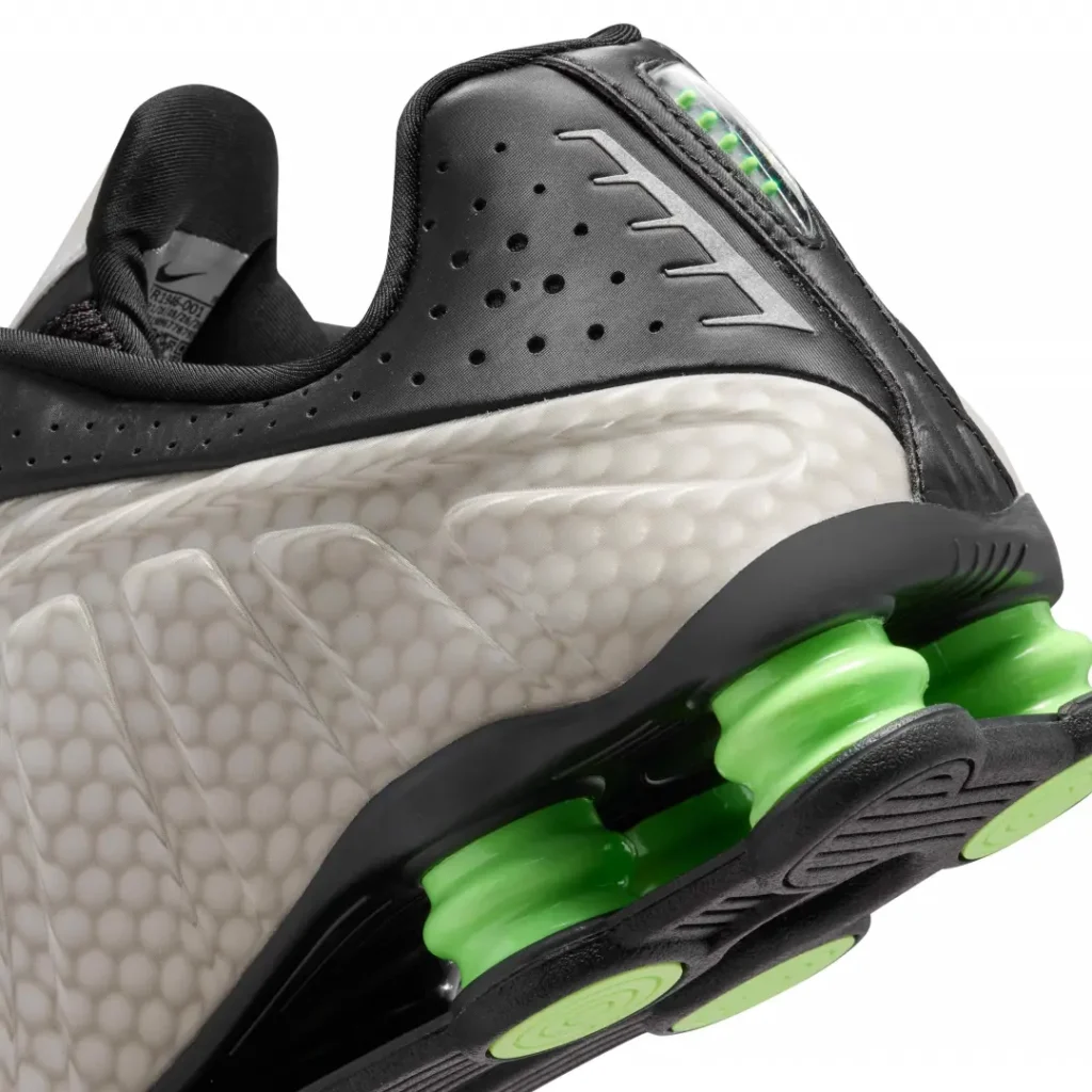 Close-up of the Nike Shox TL heel showing perforated black leather, reflective heel accents, textured sidewall, and green Shox cushion