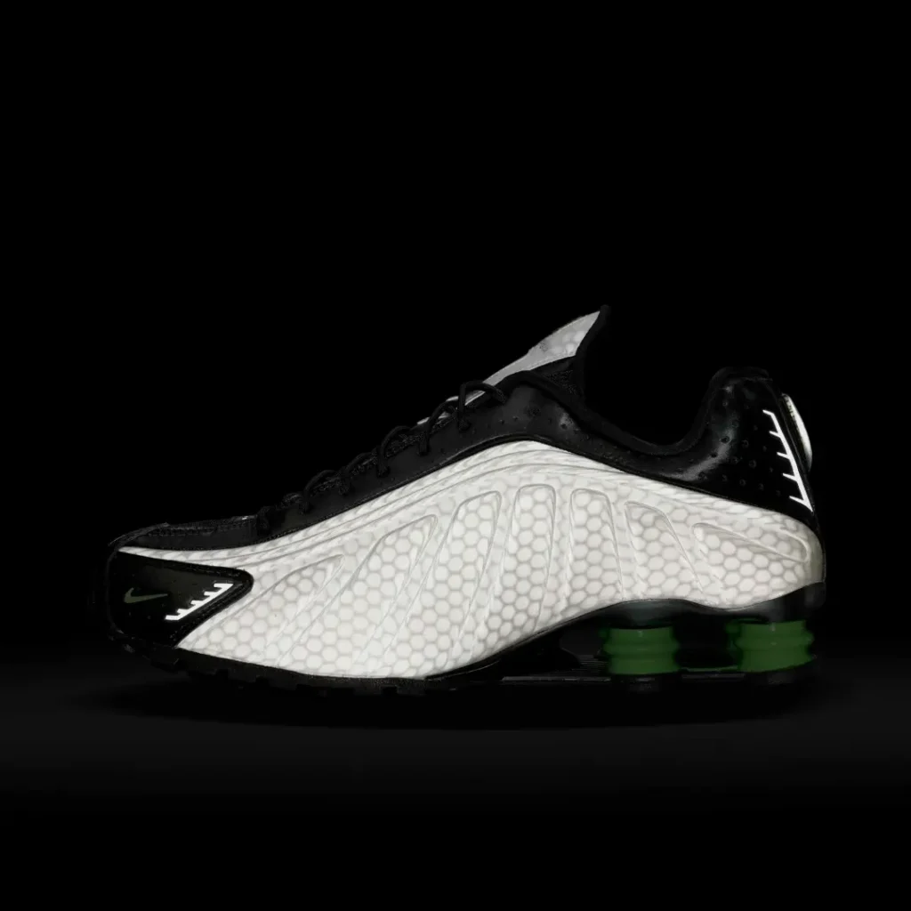 Studio profile of the Nike Shox TL against a black background emphasizing the luminous pearl gray upper and vivid green Shox column