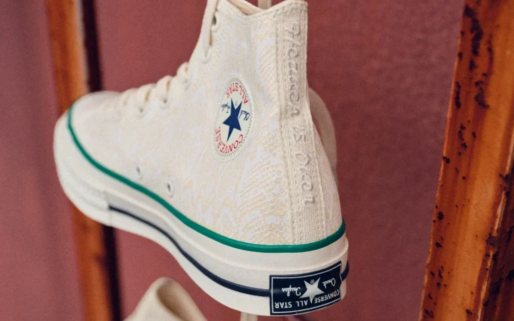 Rear three-quarter view of the cream Converse Chuck Taylor All Star high-top showcasing the embroidered heel branding, tonal graphic canvas, green foxing stripe, and Converse All Star heel license plate