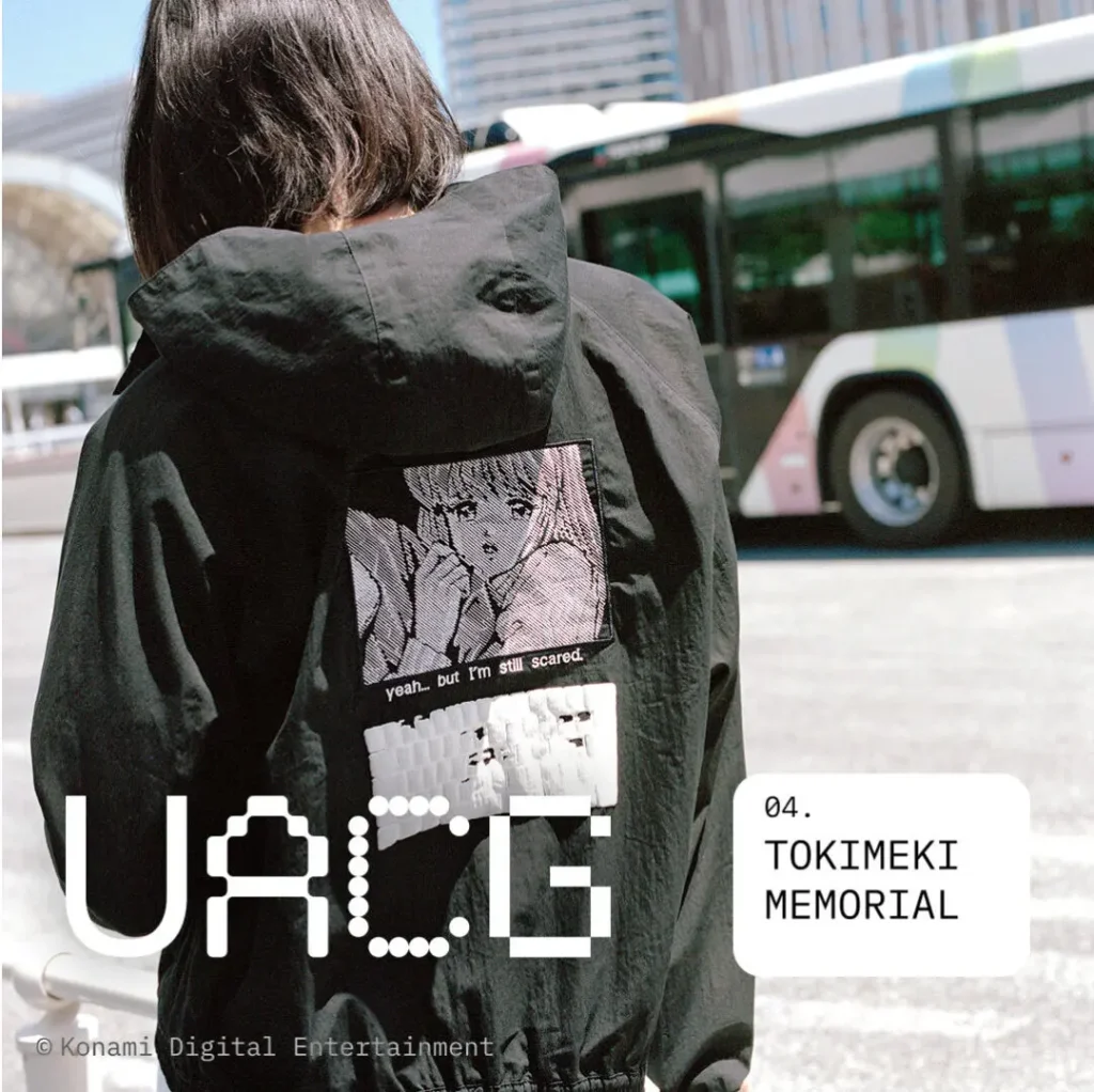 Person wearing a black hooded jacket with a large manga-inspired back graphic and subtitle text, photographed on a city street with a bus in the background