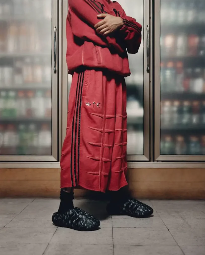 Campaign image of a model wearing red adidas Originals by Taqwa Bint Ali apparel paired with the graphic-print Adistar Cushion Mule