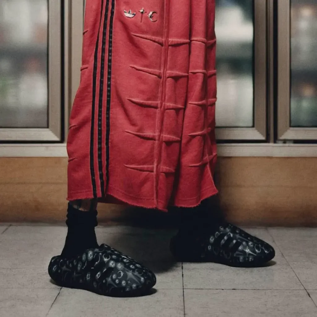 Close-up of the red adidas Originals by Taqwa Bint Ali sculpted shorts paired with the graphic-print Adistar Cushion Mule