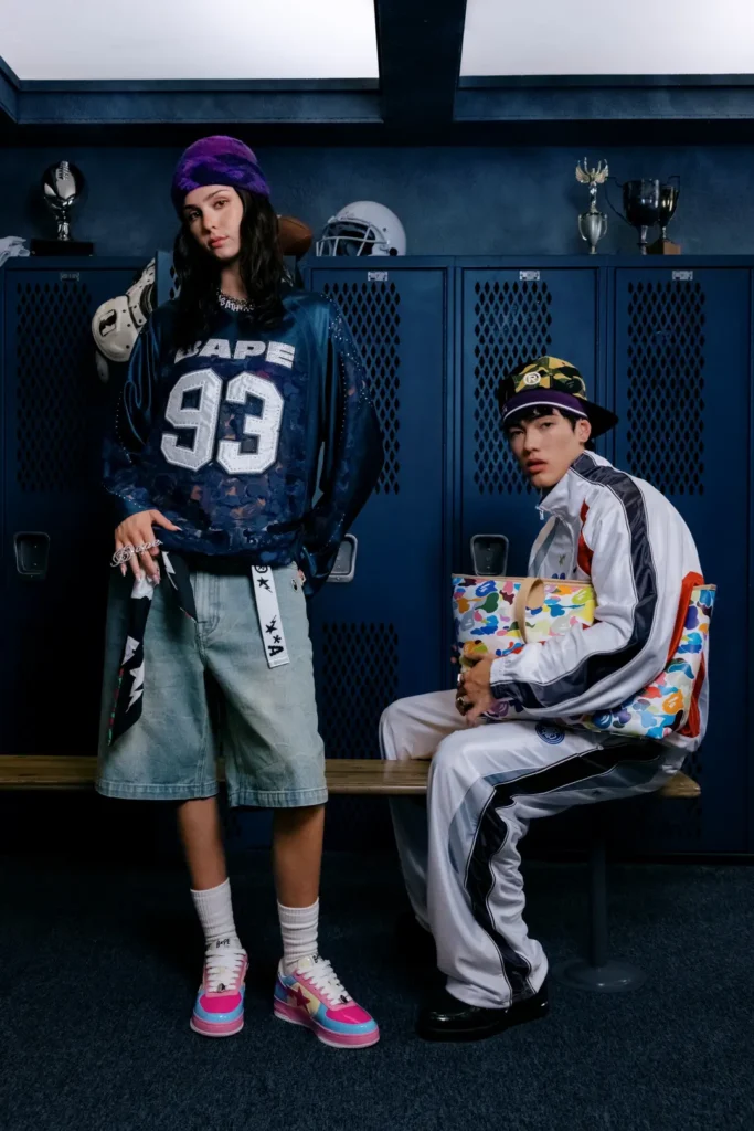 Two models in a locker room featuring a navy BAPE football jersey, pastel sneakers, white tracksuit, camouflage tote bag, and purple knit beanie