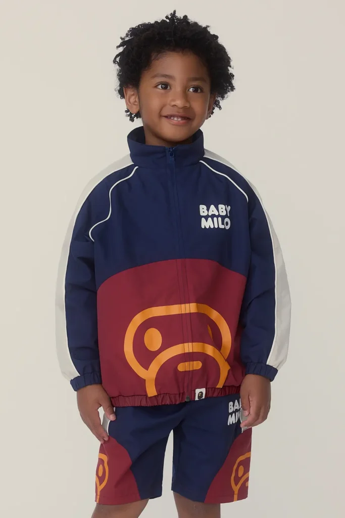 Smiling child in a navy and burgundy Baby Milo tracksuit featuring oversized monkey graphics with matching athletic shorts in a clean studio set