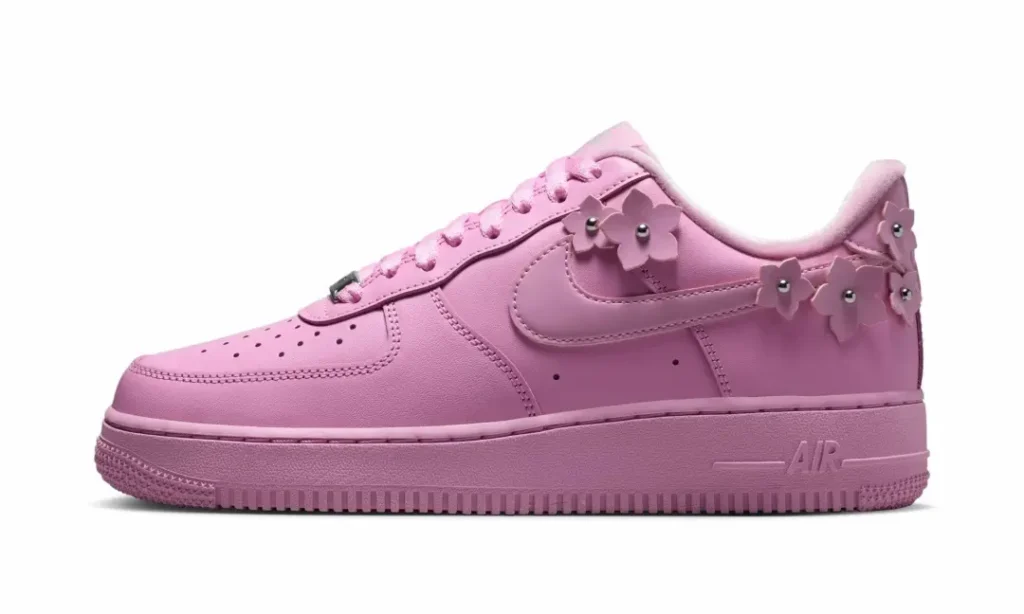 Side profile of a pastel pink Nike Air Force 1 with tonal leather construction and decorative pink flower charms along the Swoosh
