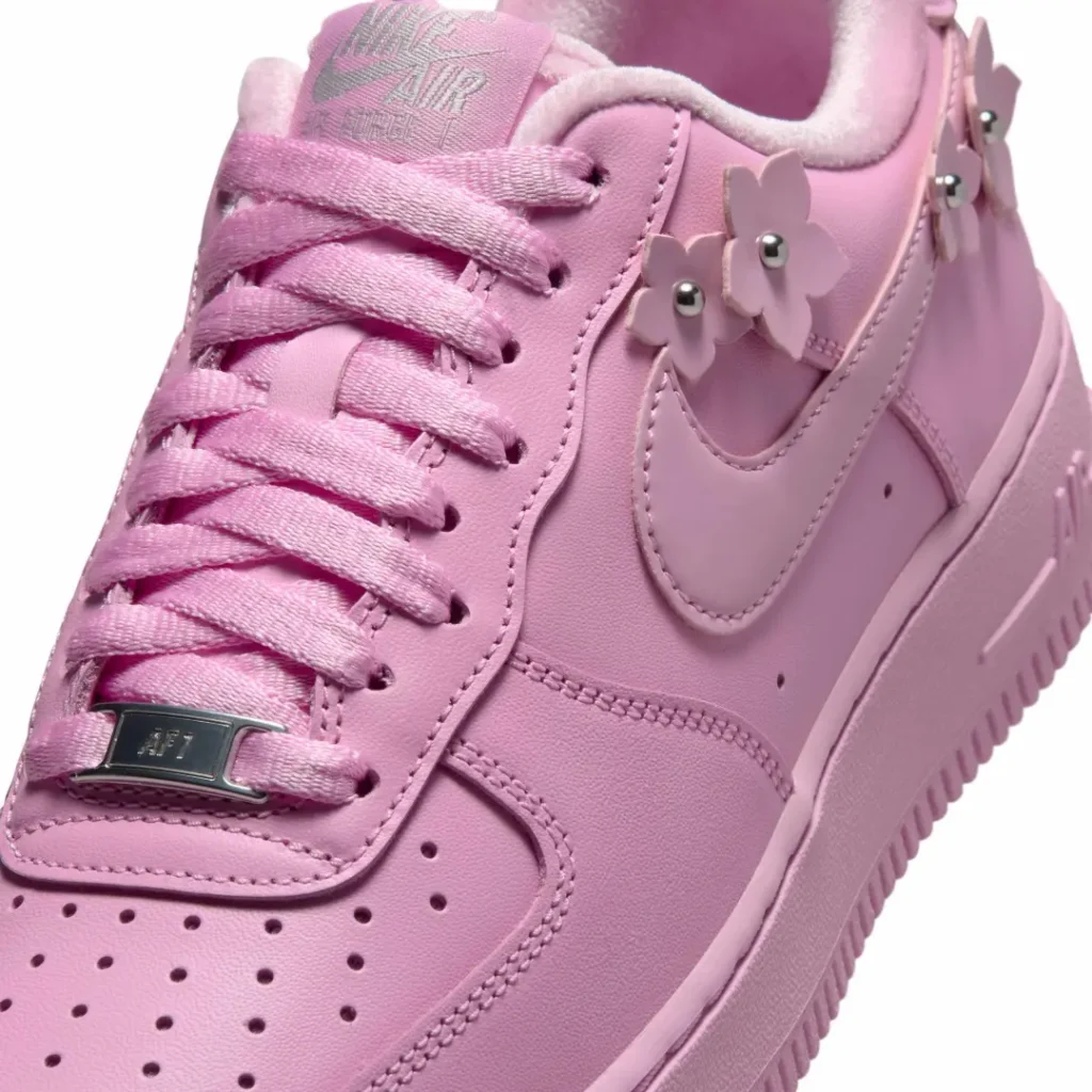 Close-up of the pastel pink Nike Air Force 1 tongue, laces, and Swoosh accented by removable flower lace charm