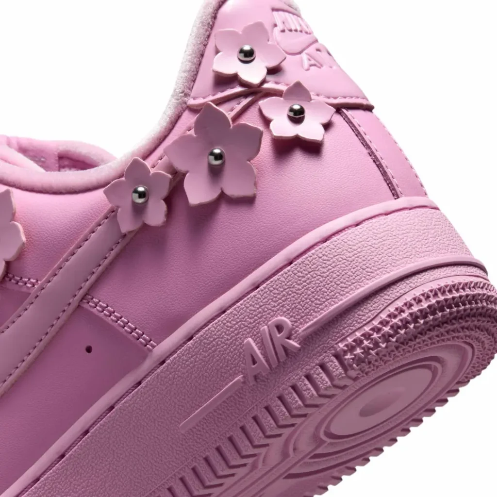 Close-up of pastel pink flower lace charms with silver stud centers decorating the side of a Nike Air Force 1