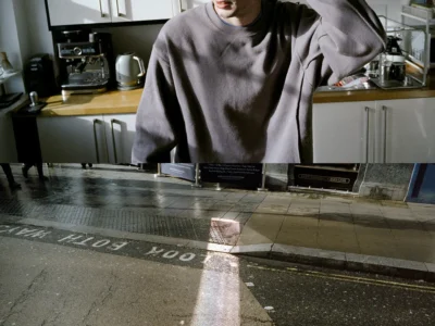 Split-frame fashion image showing a male model in a gray C.P. Company-style sweatshirt standing in a sunlit kitchen above a rain-darkened London street marked “LOOK RIGHT.”