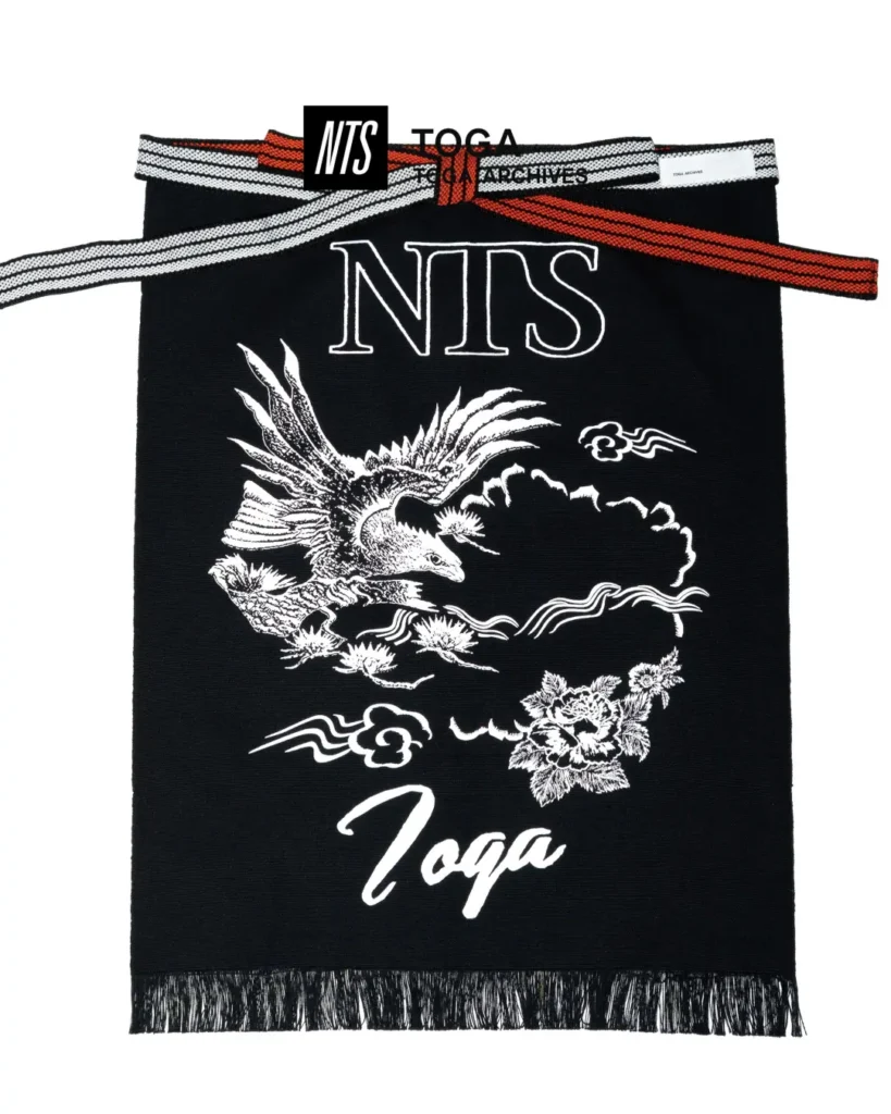 Black knit scarf with large NTS and TOGA logos, eagle and floral artwork, striped straps, and fringed hem