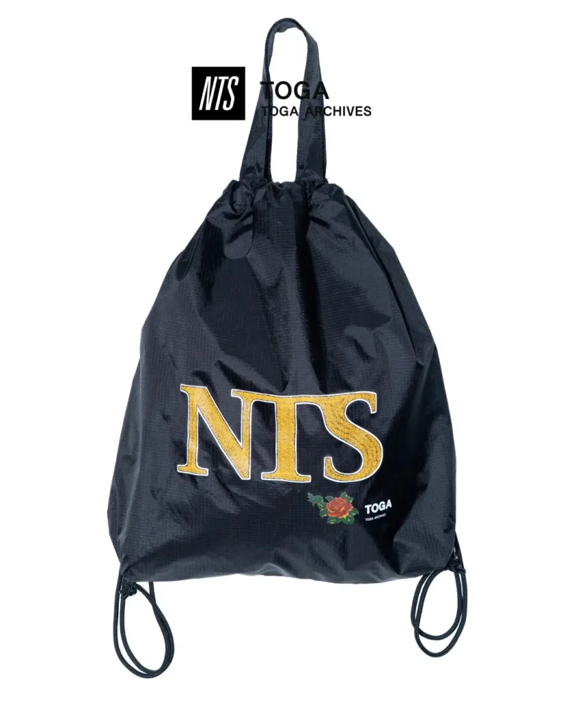 Black ripstop drawstring tote bag with oversized gold NTS logo, floral graphic, TOGA brand, and dual carry handle