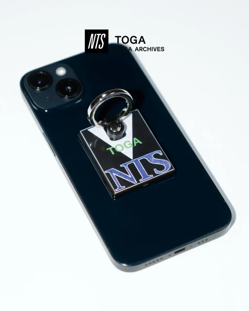 Black NTS x TOGA metal phone ring attached to the back of a dark smartphone