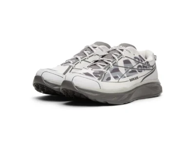 Angled front three-quarter view of a pair of white and gray HOKA running shoes on a white background, highlighting the oversized side graphics, reinforced toe caps, padded collars, reflective-style laces, and chunky cushioned midsole