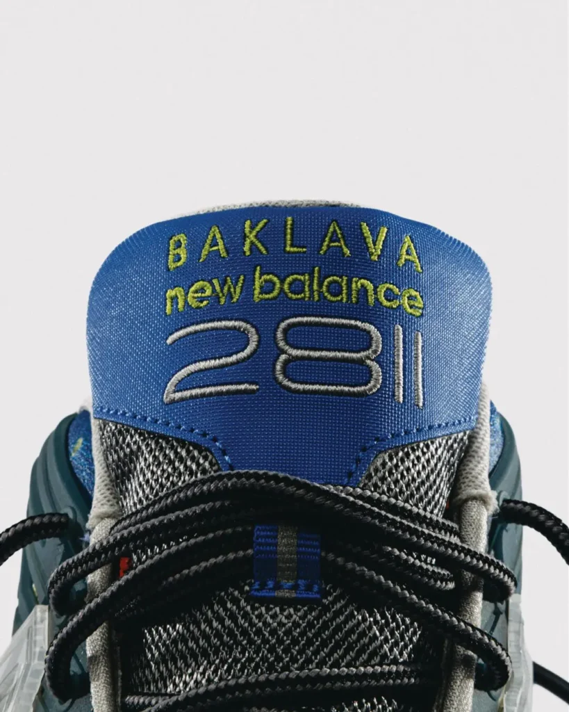 Close-up of the blue tongue embroidered with "BAKLAVA new balance 281," framed by black rope laces and grey mesh line