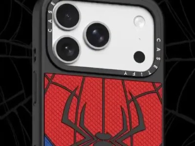 Angled close-up of the Spider-Man themed CASETiFY phone case highlighting its textured red web pattern, matte black spider emblem, blue lower side accents, black protective frame, and precision camera cutout with branded camera ring