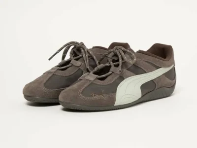 Three-quarter view of the PUMA low profile sneakers highlighting soft taupe suede overlays, dark mesh base, cream Formstrips, rope lacing system, and minimalist indoor studio set