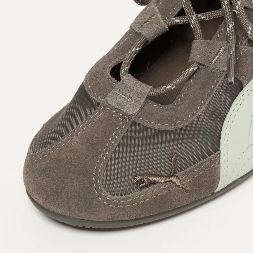 Detailed close-up of the forefoot featuring taupe suede overlays, fine mesh textile, embroidered PUMA cat logo near the toe, reinforced lace loops, and textured stitch