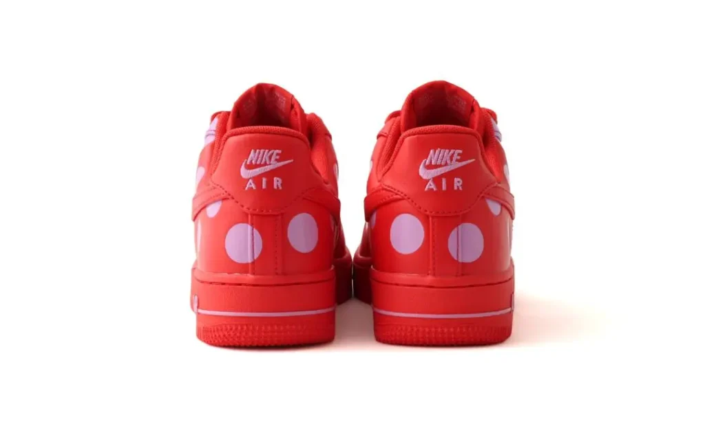 Rear view of the red Nike Air Force 1 Low sneakers with pastel pink polka dots wrapping around the heel panels, white Nike Air heel branding, and a solid red midsole displayed against a white background