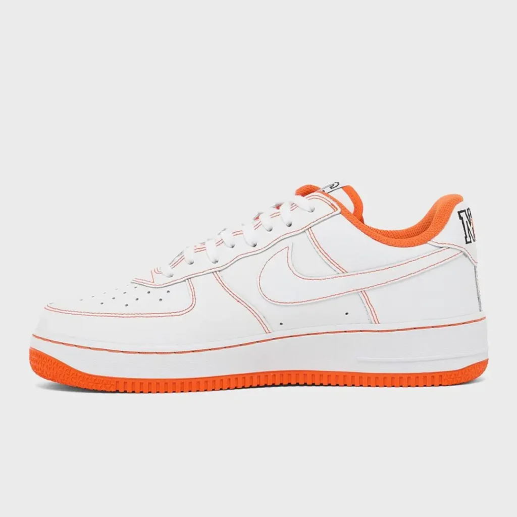 Lateral profile of the Nike Air Force 1 Low in white leather with orange contrast stitching, orange collar lining, white Swoosh, embossed midsole signature detail, and bright orange outsole