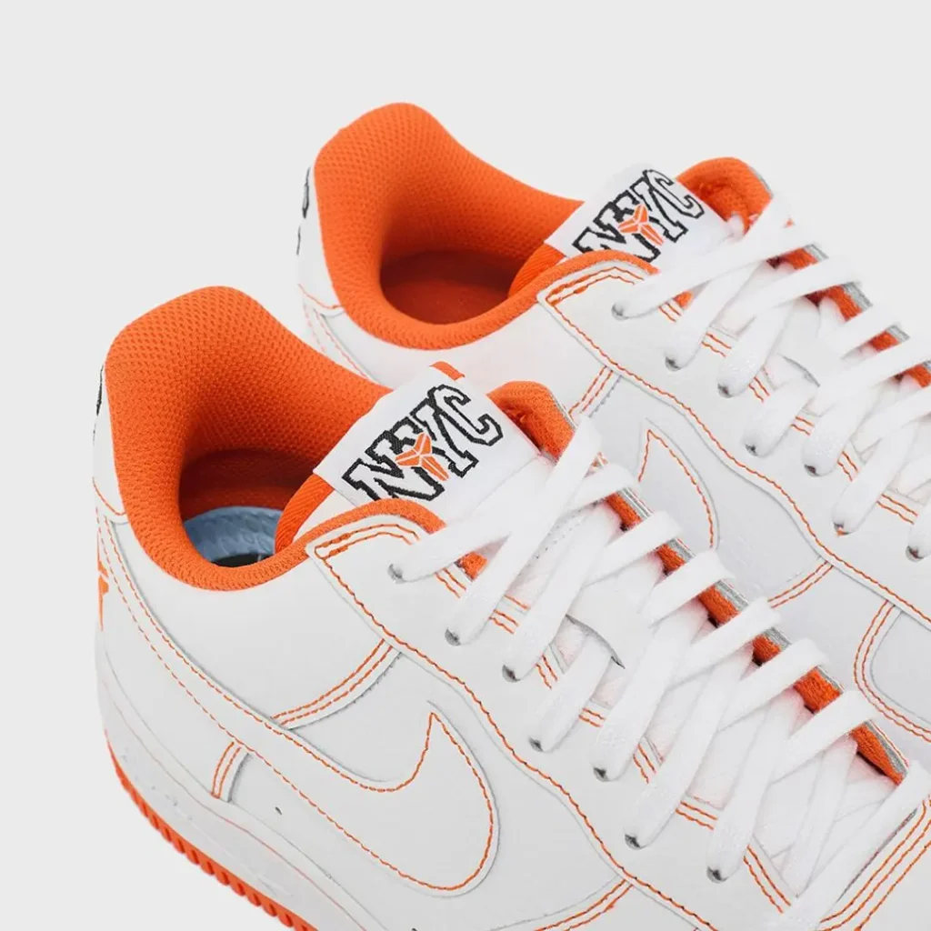 Close-up of the upper showcasing the white leather construction, orange contrast stitching, white Swoosh, NYC tongue branding, white laces, and vivid orange padded collar