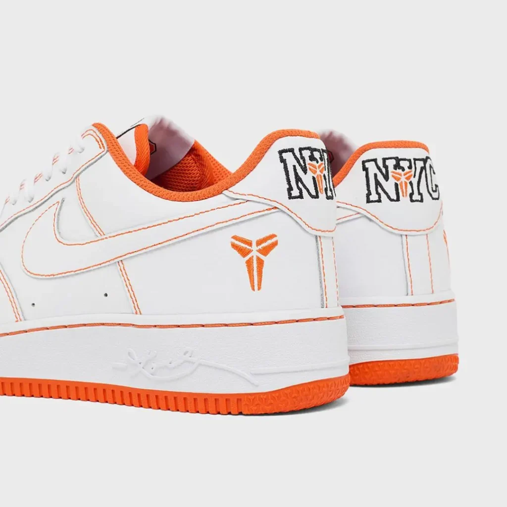 Rear three-quarter view highlighting embroider orange Kobe logos on the lateral heels, NYC heel branding, embossed signature on the midsole, and bright orange outsole