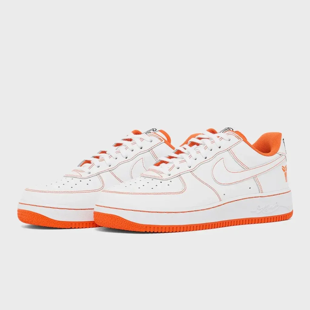 Pair of white leather Nike Air Force 1 Low shoe displayed side by side, showcasing orange contrast stitching, orange lining, Kobe logo embroidery on the heel, and bright orange rubber outsole
