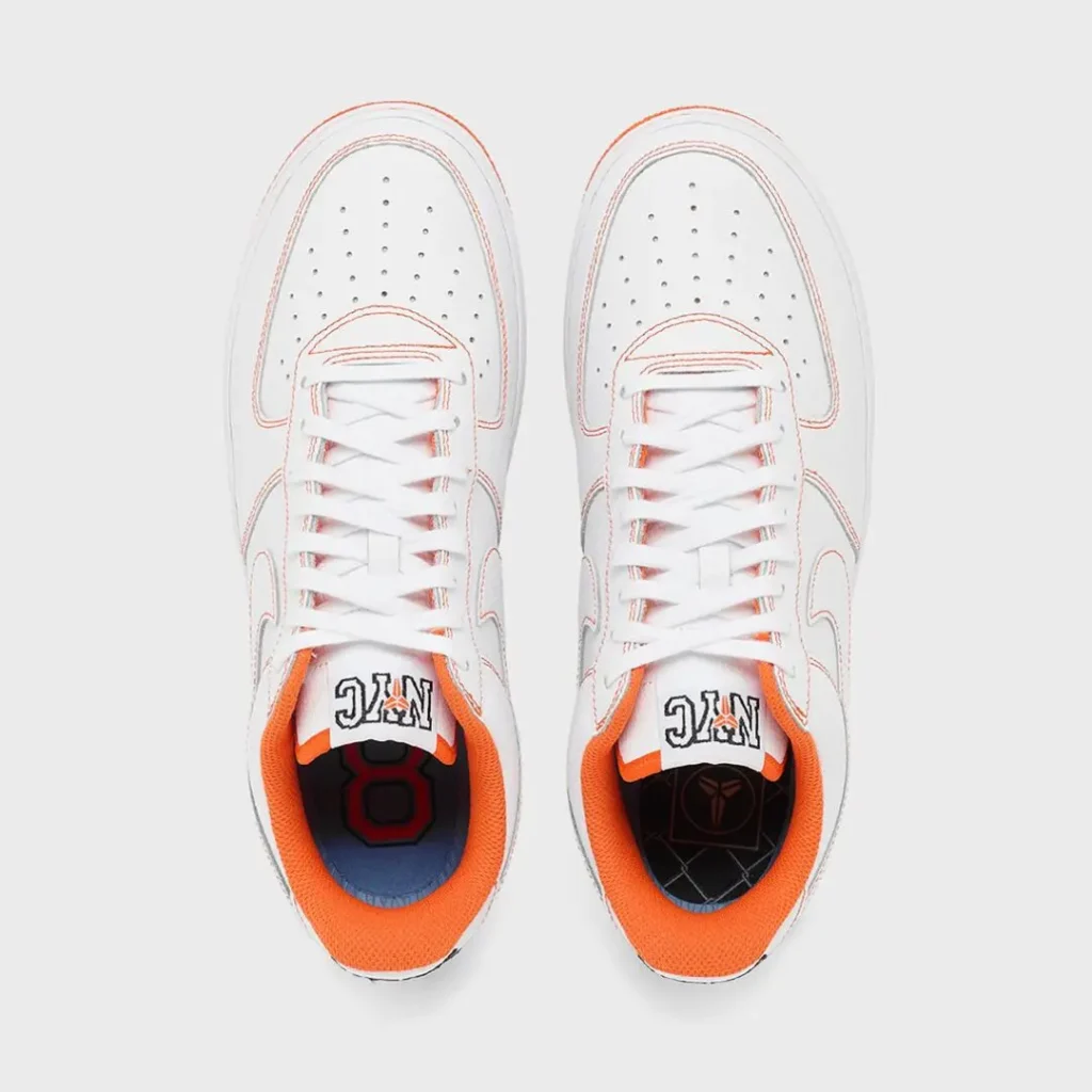 Top-down view of the Nike Air Force 1 Low highlighting white flat laces, perforated toe boxes, orange interior lining, NYC-branded tongue labels, and custom graphic insole