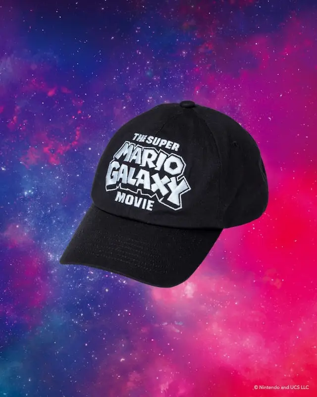 Black baseball cap from the BEAMS × Super Mario collection embroidered with 'The Super Mario Galaxy Movie' logo across the front, photographed against a colorful galaxy-inspired background.