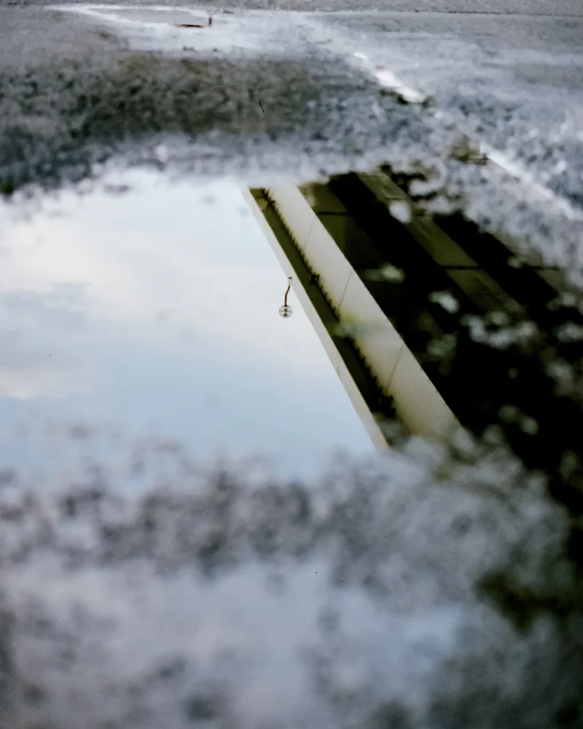 Abstract reflection of an urban structure and hanging light captured in a rain puddle, creating a minimalist composition with soft focus and muted tone