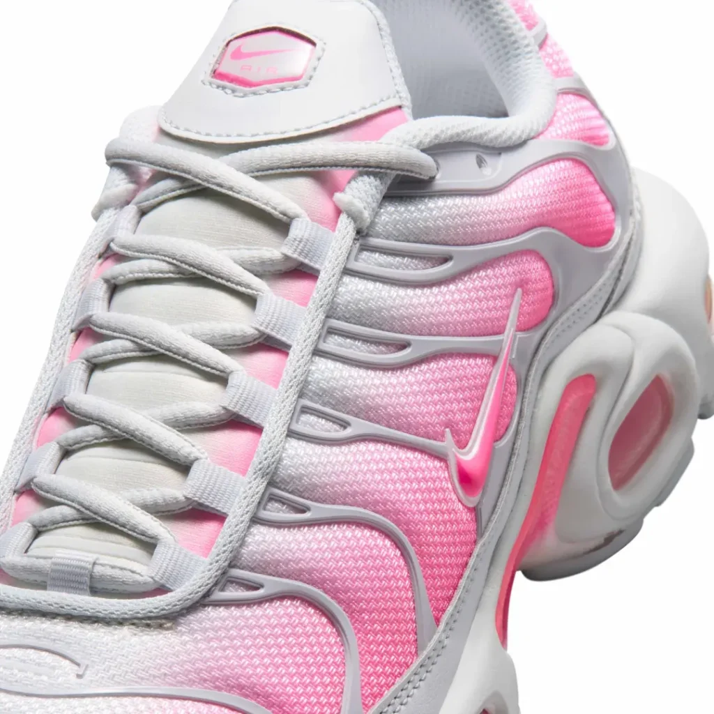 Close-up of the Air Max Plus upper featuring textured mesh, gray TPU wave overlays, and glossy pink Swoosh brand