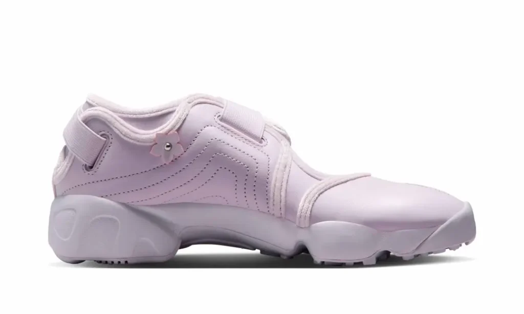 Soft pastel pink Nike Air Rift shown in profile featuring the signature split toe, adjustable hook-and-loop straps, floral appliqués with metallic studs, and sculpted midsole