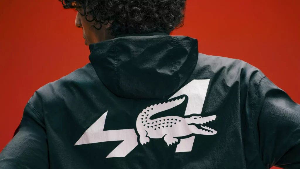 Close-up of the Alpine A290 Rallye racing seatbacks with geometric mesh construction, red Lacoste-branded harnesses, Alpine "A" logos, and embossed crocodile emblem