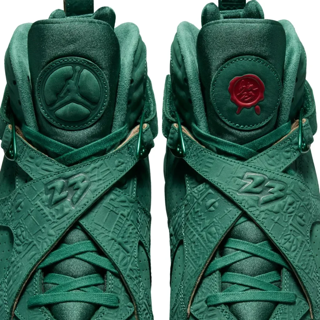 Close-up of the Air Jordan 8 x SoleFly tongues showing an embossed Jumpman logo on one shoe and a red wax seal-inspired SoleFly emblem on the other above the crossover strap