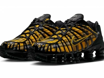 Pair of Nike Shox sneakers featuring a yellow and black tartan plaid textile upper, black TPU cage overlays, glossy black Shox cushioning columns, and embroidered yellow Swoosh