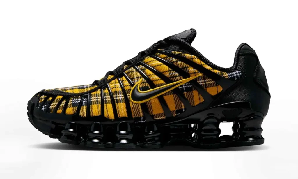 Lateral side view of the Nike Shox sneaker showcasing a yellow tartan plaid upper, black TPU cage, embroidered yellow Swoosh, and glossy black Shox sole