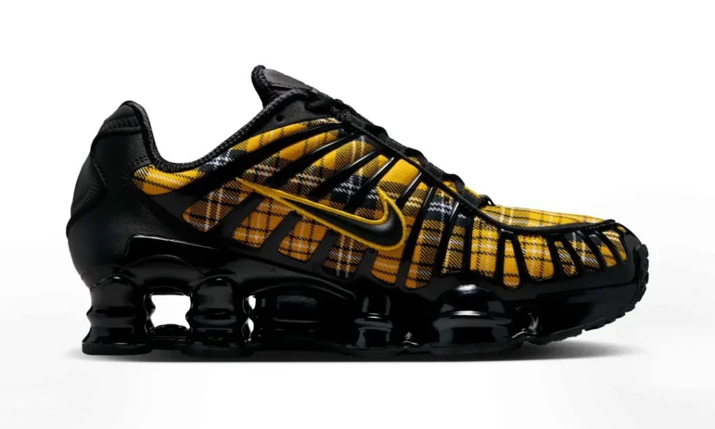 Medial side view of the Nike Shox sneaker with a yellow tartan plaid upper, black TPU support cage, and glossy black Shox cushion sys