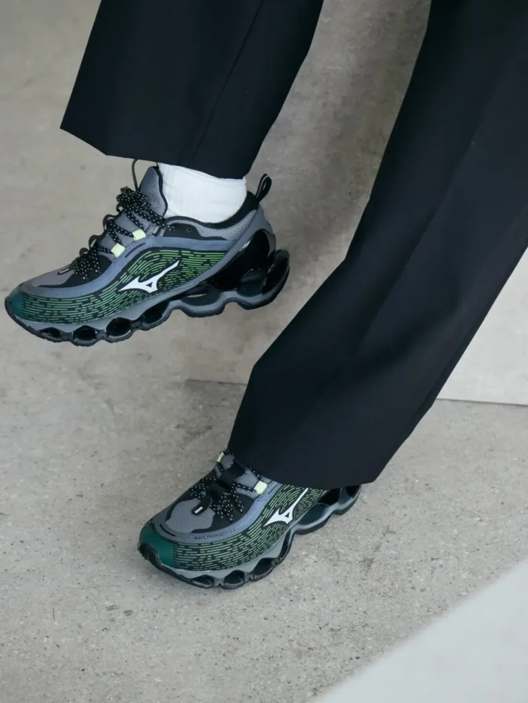 Close-up of black pants and white socks paired with black, gray, and green Mizuno sneakers on concrete pavement