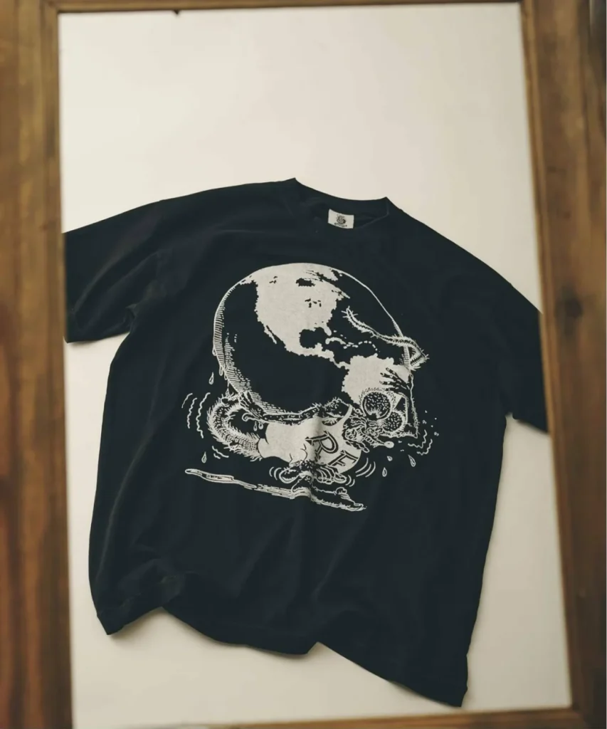 Black short sleeve Tee on display, screen printed with a monster face wrapped around a globe/skull graphic with dripping details and partial "RF" letter