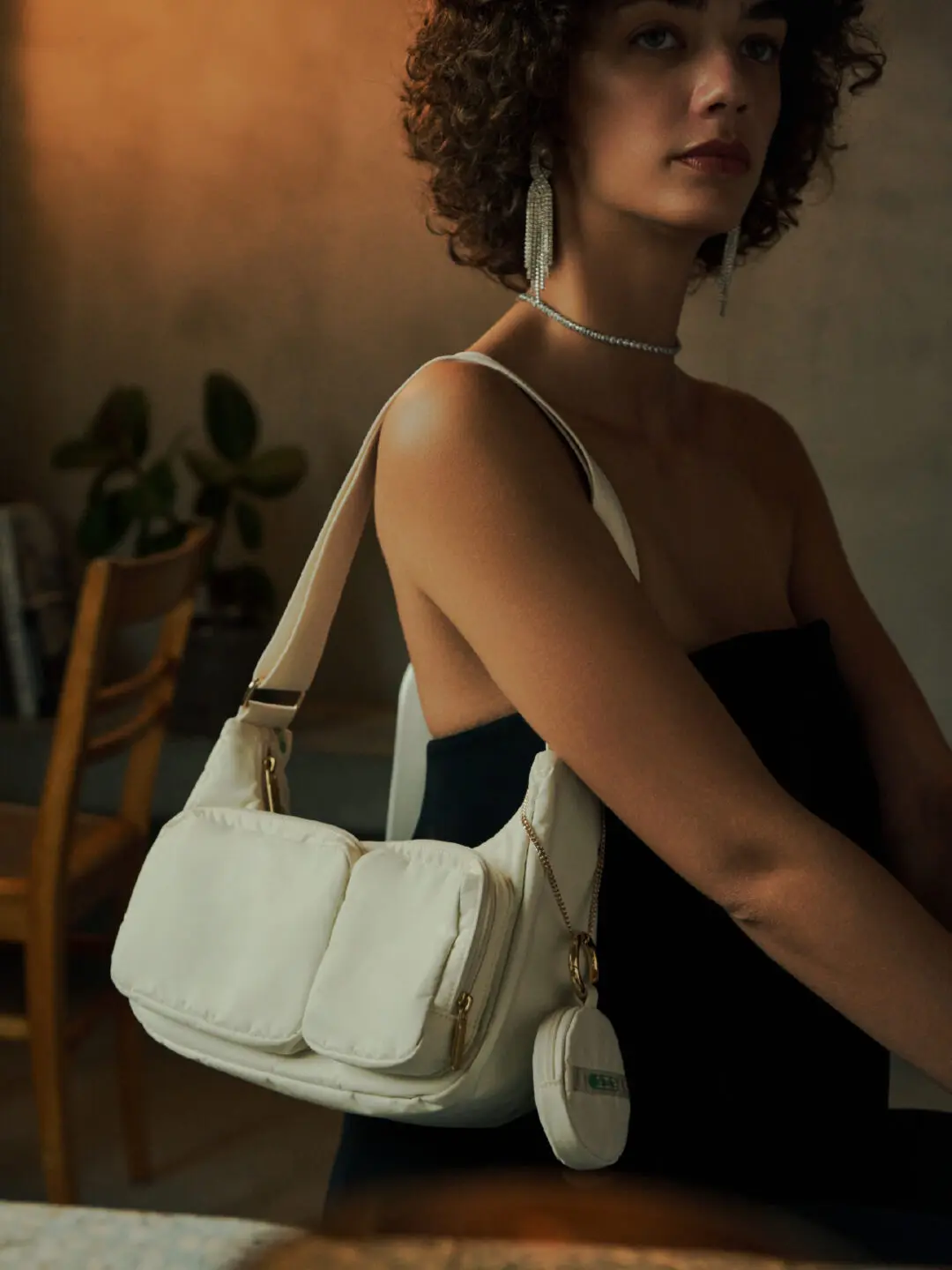 Model wearing a black evening dress accessorized with a white LeSportsac shoulder bag featuring oversized padded utility pockets, gold-tone hardware, and a matching round zip pouch.